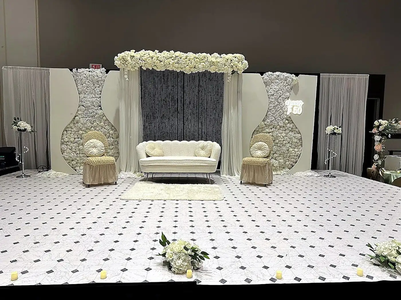 White floral wall milestone celebration stage with beaded backdrop, ivory loveseat and marble dance floor by Bsquare Events