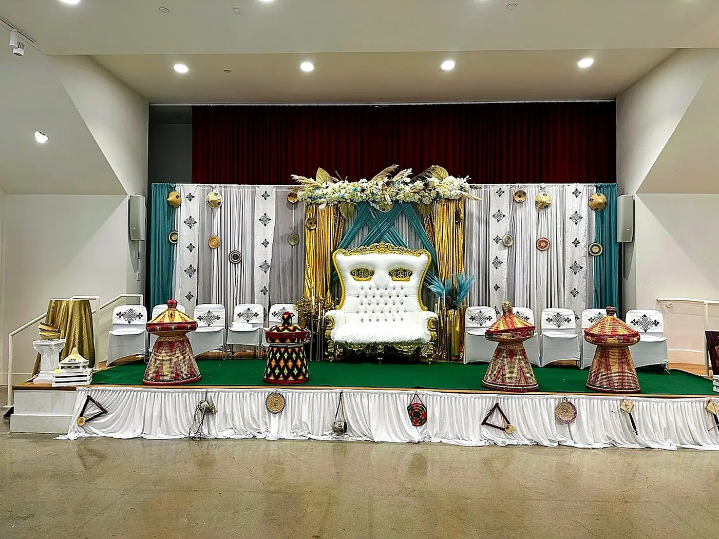 Traditional Ethiopian wedding stage with teal and gold draping, woven mesob baskets and a white throne by Bsquare Events