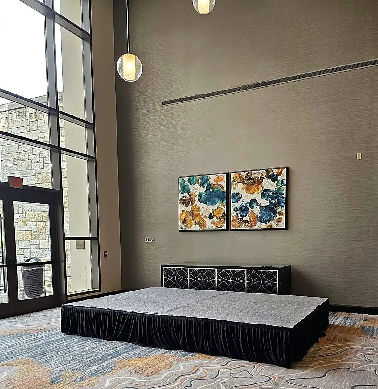 Carpeted modular stage rental platform with black skirting set up in a hotel foyer by Bsquare Events