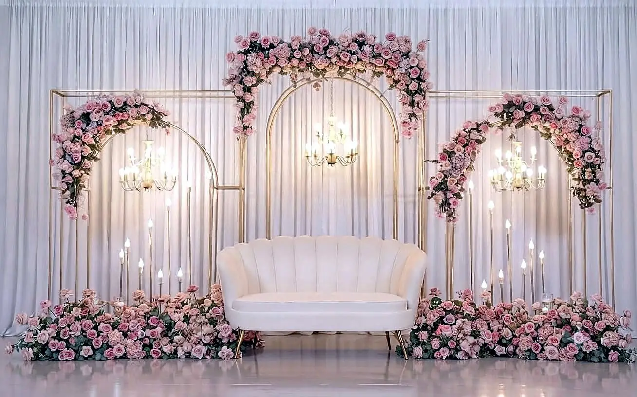 Ivory velvet couch setup with gold arches, blush rose florals and chandeliers on a white drape backdrop by Bsquare Events