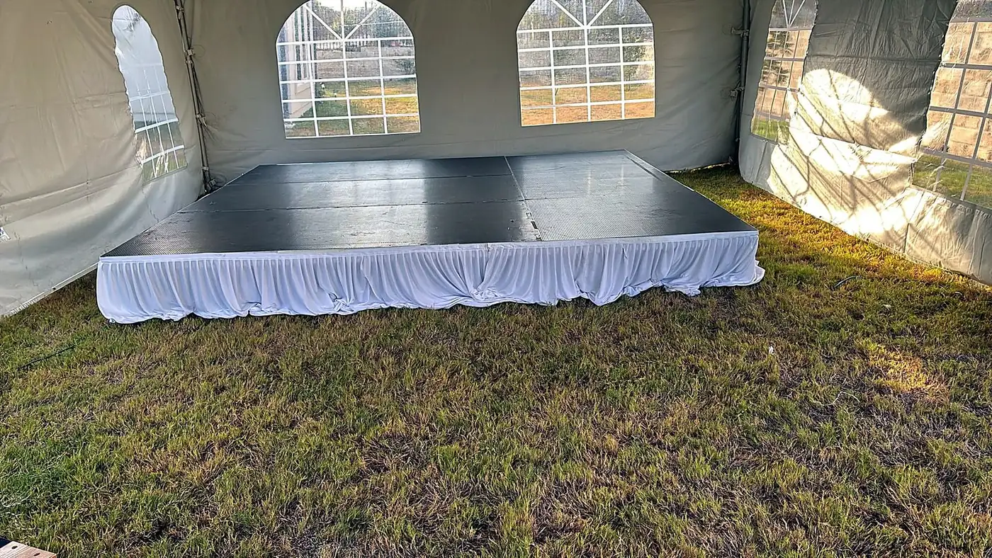 Modular event stage with white skirting set up inside a marquee tent on grass by Bsquare Events